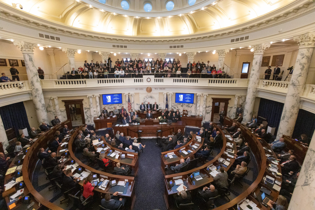 A wide view of a legislative chamber with officials seated at curved desks showcases what we do—governing under the watchful gaze of an audience in the gallery above, surrounded by ornate pillars and a domed ceiling illuminating the room. | Living with Wolves